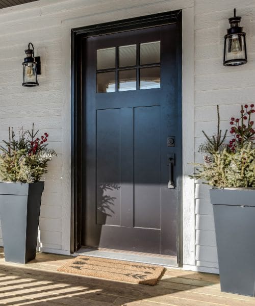 Black front door with glazed top panels and planters either side